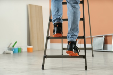 Person climbing ladder indoors, closeup on feet. Space for text