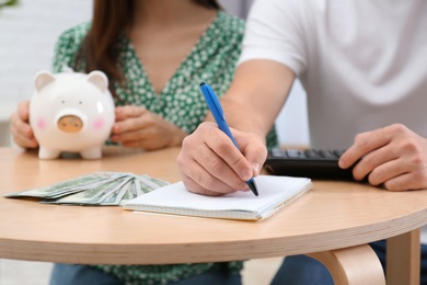 Young couple with piggy bank and money at table, closeup