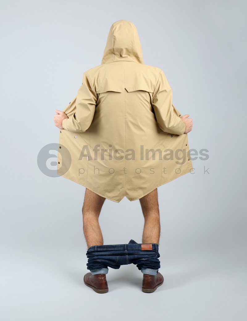 Exhibitionist exposing naked body under coat on light background, back view