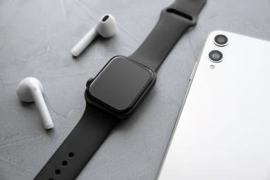 Stylish smart watch, phone and earphones on grey stone table, closeup