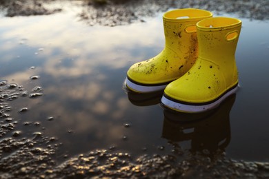 Yellow rubber boots in puddle outdoors, space for text. Autumn walk