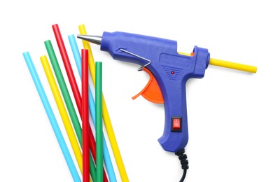 Blue glue gun and colorful sticks on white background, top view