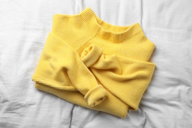 Photo of Yellow warm sweater on white bedsheet, top view