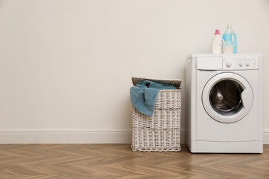 Photo of Laundry room interior with modern washing machine and wicker basket near white wall. Space for text
