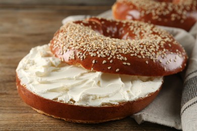Delicious bagel with cream cheese on wooden table, closeup