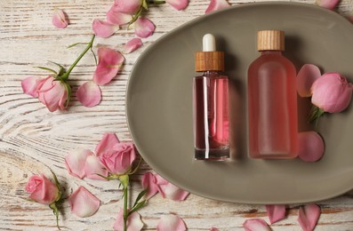 Flat lay composition with essential rose oil and flowers on white wooden table