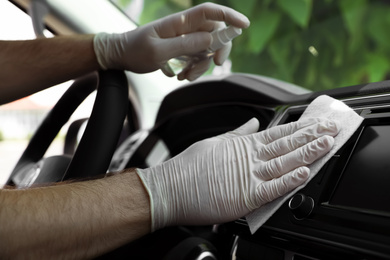 Man cleaning dashboard with wet wipe and antibacterial spray in car, closeup