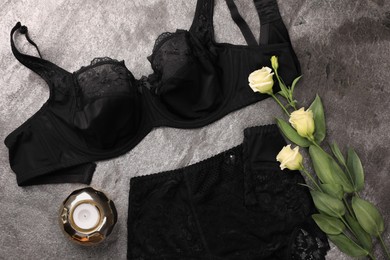 Elegant black plus size women's underwear, candle and beautiful eustoma flowers on grey background, flat lay