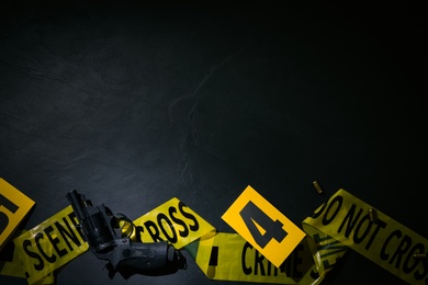 Flat lay composition with gun and crime scene marker on black slate background. Space for text