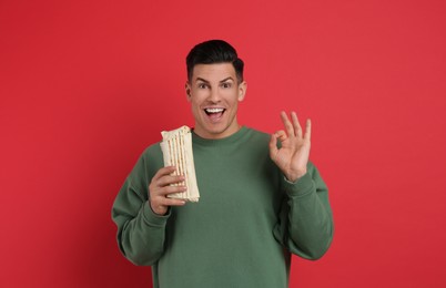 Excited man with delicious shawarma on red background