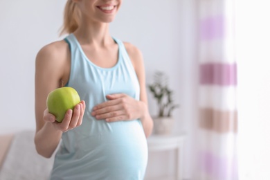 Young pregnant woman holding apple at home