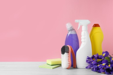 Photo of Different cleaning supplies and beautiful spring flowers on white wooden table against light pink background. Space for text