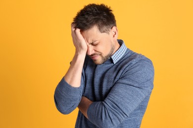 Man suffering from terrible migraine on yellow background