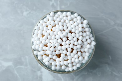 Many cotton buds in glass jar on light grey marble table, top view