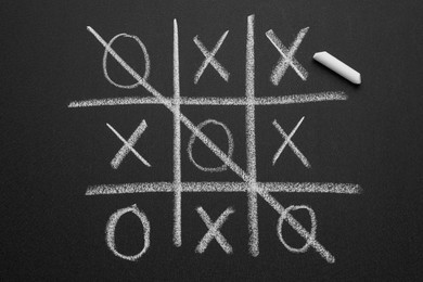 Tic tac toe game and piece of chalk on blackboard, top view