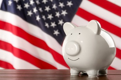 Photo of Piggy bank on wooden table against American flag, space for text