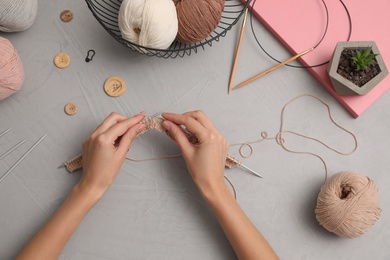 Photo of Woman knitting with threads at grey table, top view. Engaging hobby