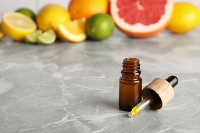 Bottle of essential oils with different citrus fruits on grey marble table. Space for text