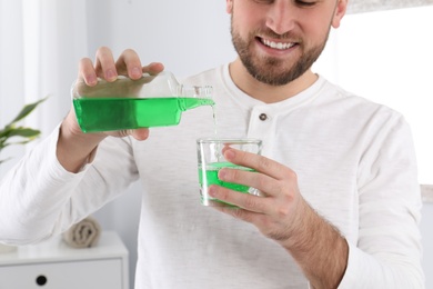 Young man with mouthwash in bathroom, closeup. Teeth and oral care