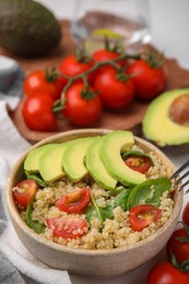 Photo of Delicious quinoa salad with tomatoes, avocado slices and spinach leaves served on table