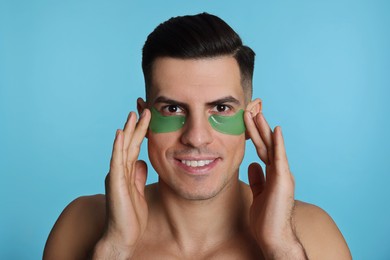 Man applying green under eye patches on light blue background