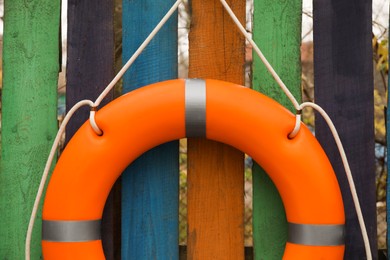 Orange lifebuoy hanging on color wooden fence, closeup. Rescue equipment