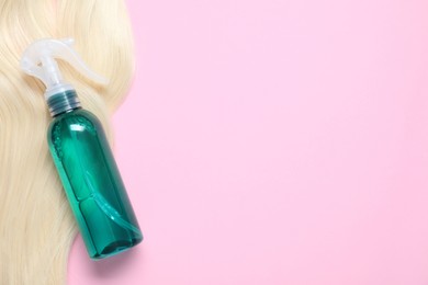 Photo of Spray bottle with thermal protection and lock of blonde hair on pink background, flat lay. Space for text