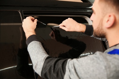 Skilled worker tinting car window in shop
