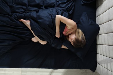 Young woman sleeping in comfortable bed with silky linens, top view
