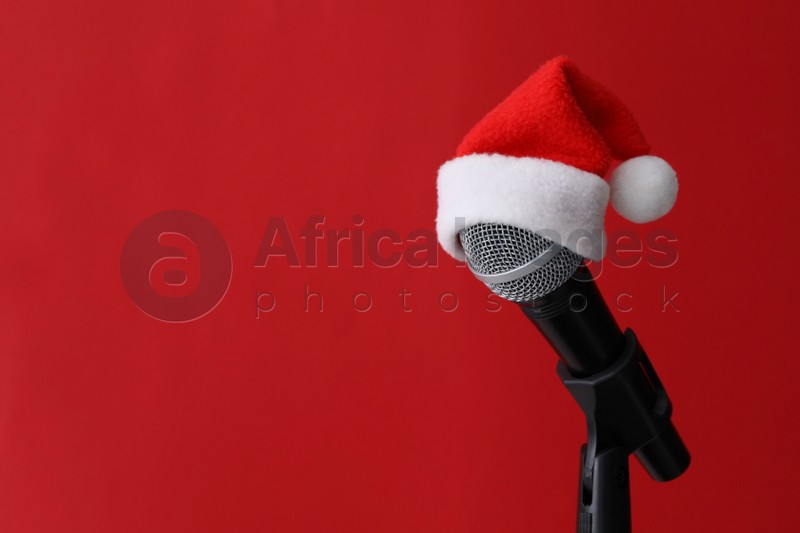 Microphone with Santa hat on red background, space for text. Christmas music