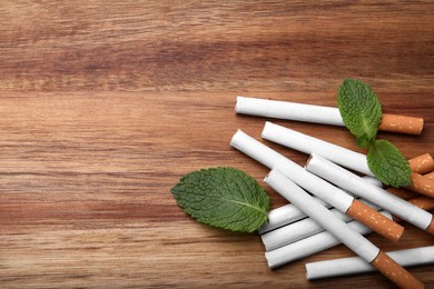 Menthol cigarettes and mint leaves on wooden table, flat lay. Space for text