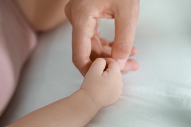 Baby holding motherʼs hand on bed, closeup