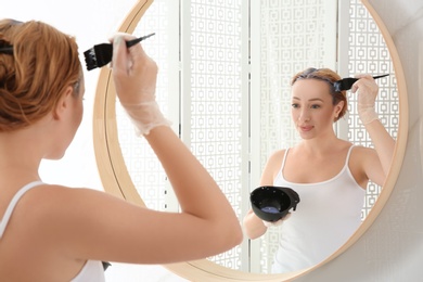 Young woman applying hair dye on roots in front of mirror at home