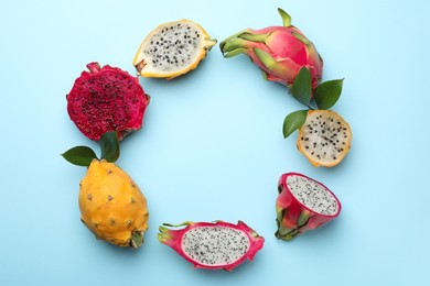 Frame of delicious cut and whole dragon fruits on light blue, flat lay. Space for text