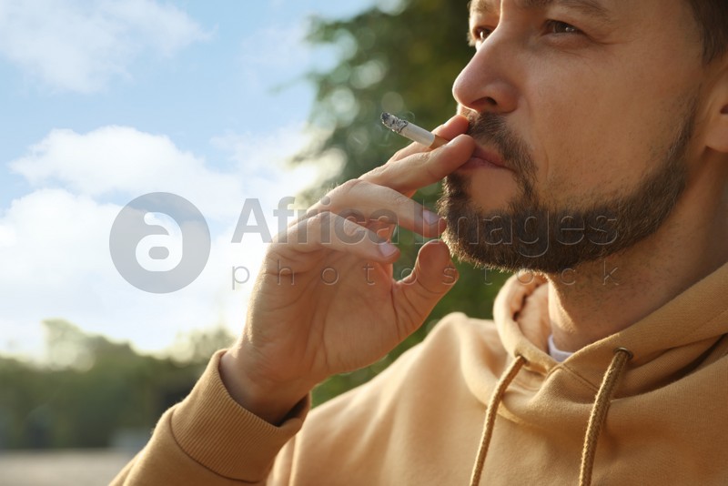 Handsome mature man smoking cigarette outdoors, closeup