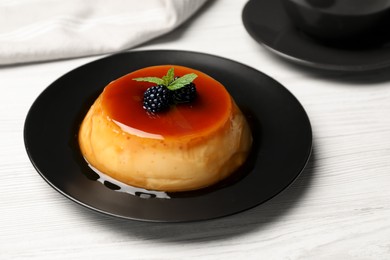 Photo of Plate of delicious caramel pudding with blackberries and mint on white wooden table