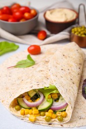 Delicious hummus wrap with vegetables on table