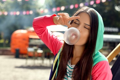 Photo of Beautiful young woman blowing chewing gum and showing peace gesture outdoors