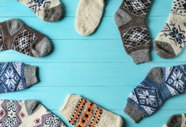 Frame made of knitted socks on light blue wooden background, flat lay with space for text. Winter clothes