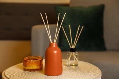 Photo of Aromatic reed air fresheners and scented candle on table indoors
