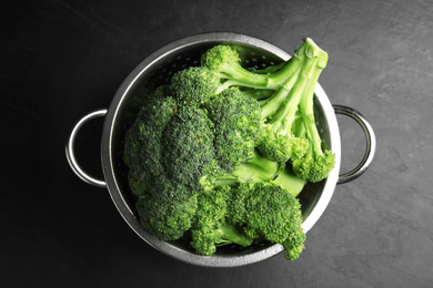 Fresh green broccoli in colander on black table, top view