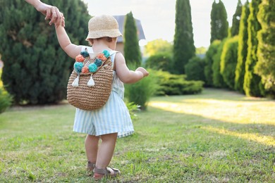 Cute little girl in stylish clothes holding mother's hand outdoors on sunny day, back view. Space for text