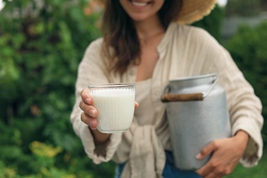Smiling woman holding can and glass with fresh milk, closeup