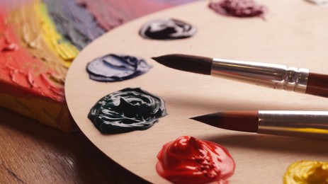 Photo of Artist's palette with samples of colorful paints and brushes on wooden table, closeup