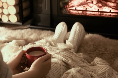 Woman with hot drink resting near fireplace at home, closeup
