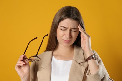 Young woman suffering from migraine on yellow background
