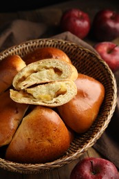 Photo of Delicious baked apple pirozhki in wicker basket and fruits on wooden table