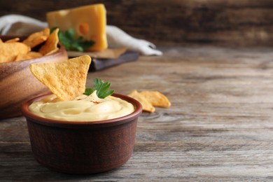 Photo of Delicious cheese sauce with nacho and parsley on wooden table, space for text