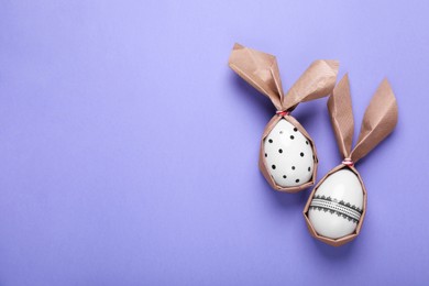 Photo of Easter bunnies made of craft paper and eggs on purple background, flat lay. Space for text