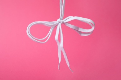 White shoe laces tied in bow on pink background